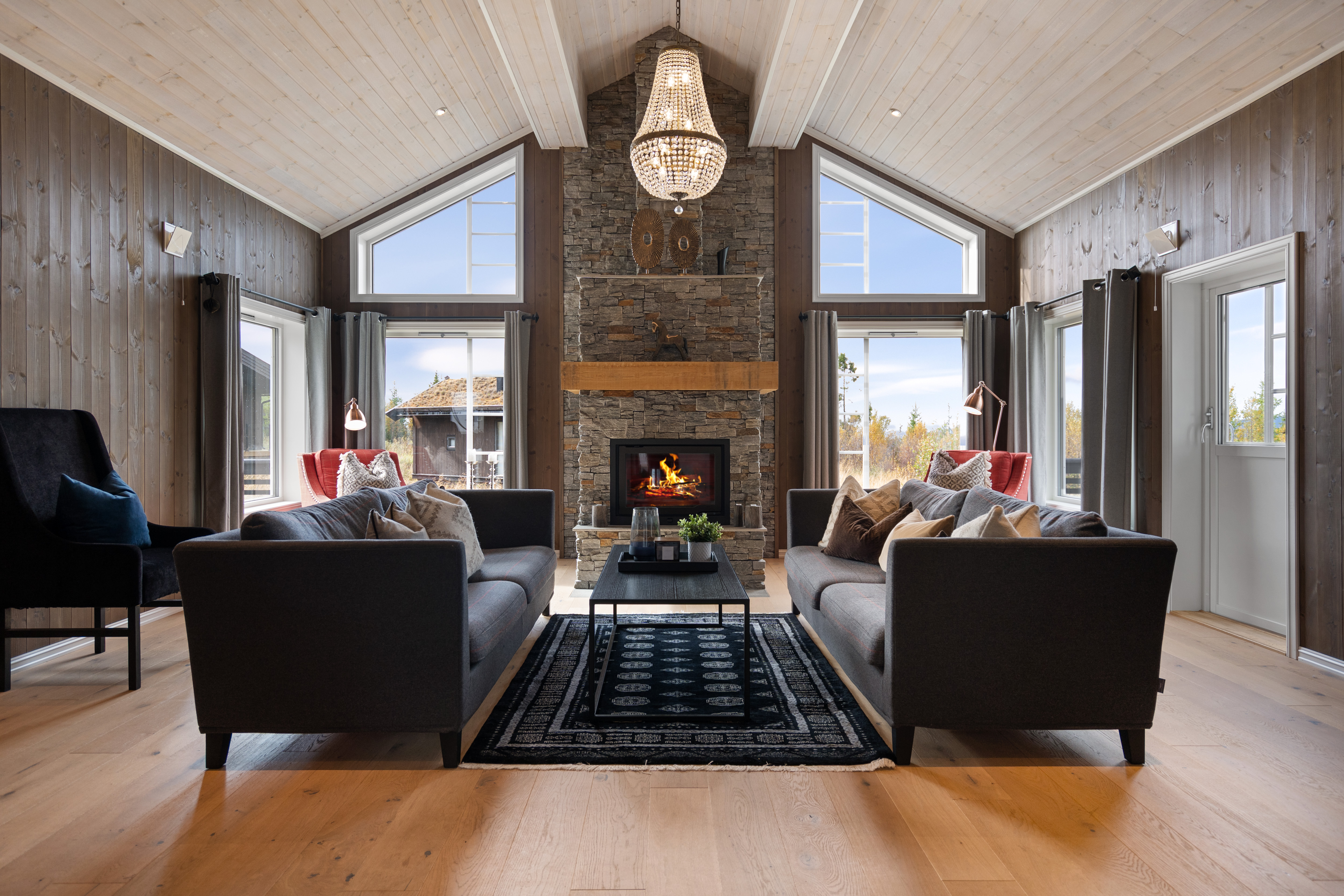 Lys og romslig stue med åpen himling, store vindusflater og peis som gir en lun atmosfære.